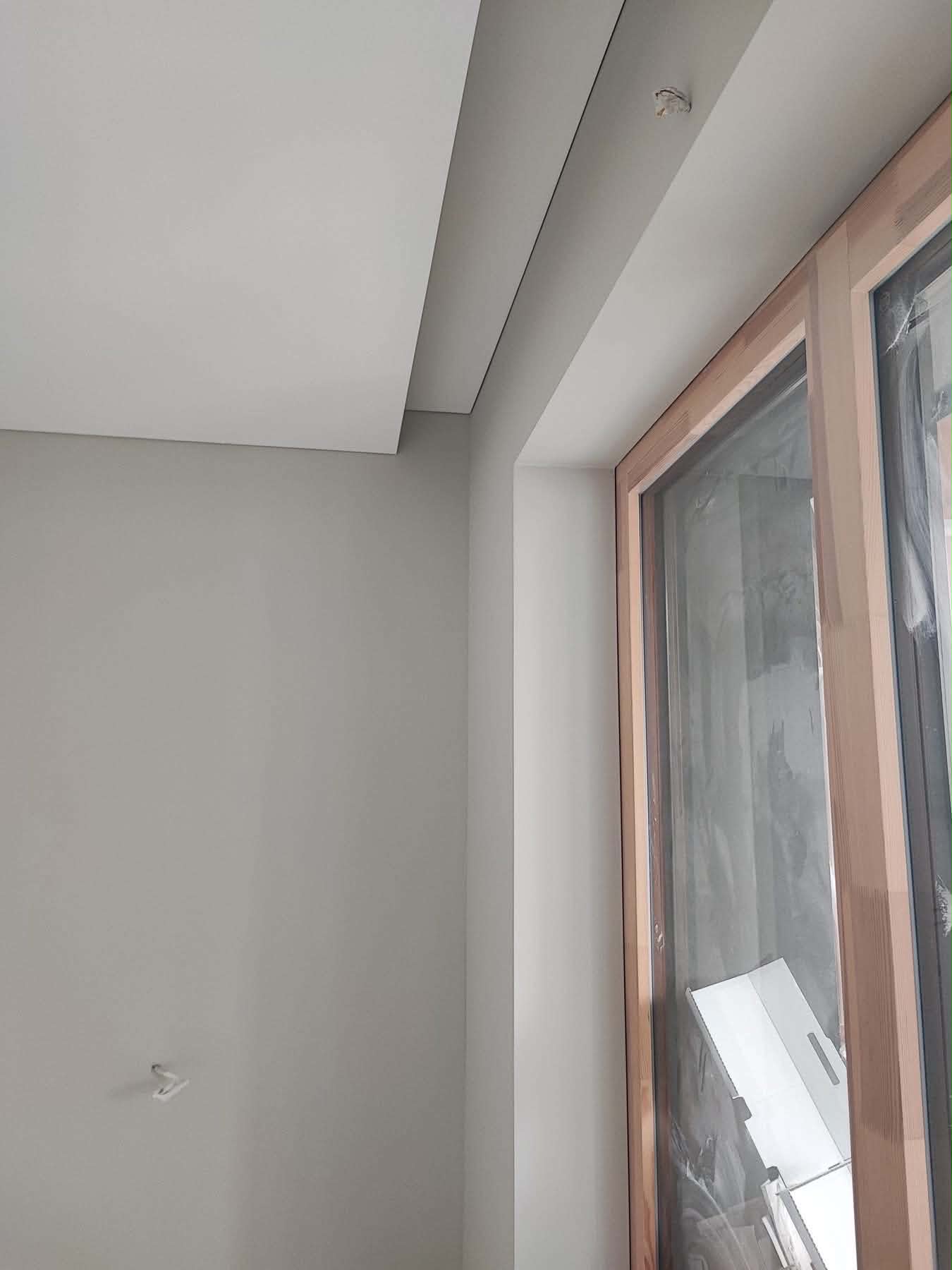Šviesus gyvenamasis kambarys Vilniuje su lygiomis baltomis sienomis po mechanizuoto glaistimo ir erdvios įtempiamų lubų sistemos montavimu